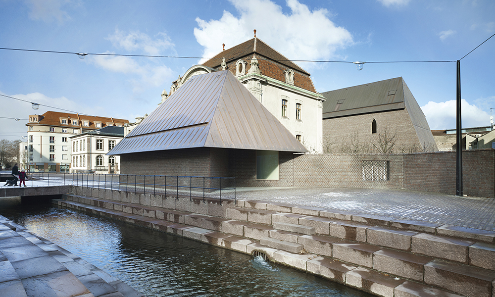 Musée Unterlinden, Colmar. Après la rénovation du musée, deux groupes de bâtiments se font face sur une place. Une nouvelle structure en brique pour les expositions (Ackerhof) et une petite maison sont reliées aux anciennes structures au niveau souterrain.