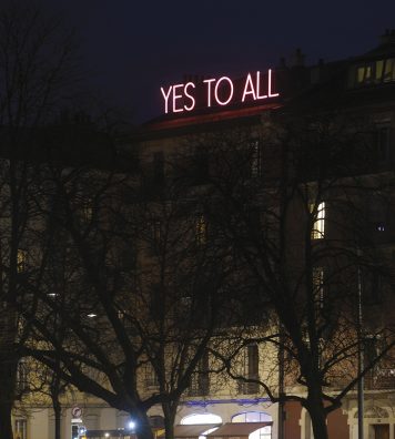 « YES TO ALL ». Lisible de tous les points de vue de la plaine de Plainpalais, le message en néon blanc entouré d’un halo rose proposé par Sylvie Fleury nous enjoint à l’optimisme.