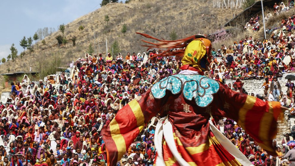 Scène de danse lors du festival annuel de Paro au Bhoutan. Un danseur mime un personnage divin devant une foule d’habitants.